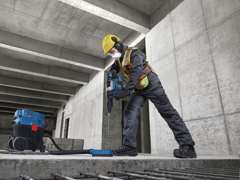 En arbejder iført sikkerhedsudstyr bruger en borehammer på et betongulv.