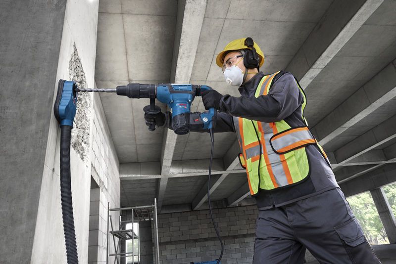 En arbejder iført sikkerhedsudstyr borer ind i en betonvæg med en borehammer.