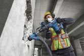 En arbejder iført sikkerhedsudstyr bruger en borehammer til at bore i en betonvæg.
