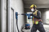 En person iført sikkerhedsudstyr bruger en borehammer til at bore i en betonvæg.