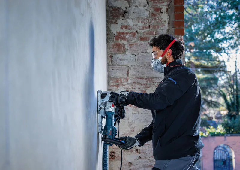 En person iført sikkerhedsudstyr betjener en vægfræser på en betonvæg.