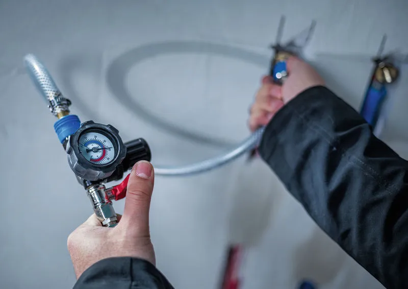 En person justerer en trykregulator, der er fastgjort til en fleksibel slange.