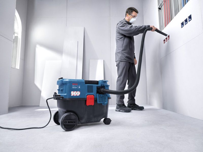 En person med sikkerhedsudstyr bruger en universalstøvsuger til at rengøre stikkontakter.