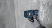 En person med sikkerhedsudstyr bruger en lasermåling på en betonvæg.