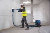 En arbejder iført sikkerhedsudstyr borer i beton med en batteridrevet borehammer.