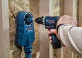 Person, der betjener en batteridrevet slagboremaskine i nærheden af ​​et støvudsugningsudstyr.