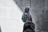 En person iført sikkerhedsudstyr bruger en lasermåler nær en betonblokvæg.