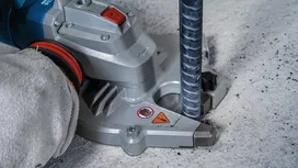 En person iført sikkerhedsudstyr borer gennem beton omkring en metalstang.