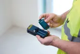 En person med sikkerhedsudstyr indsætter et batteri i en håndholdt måleenhed.