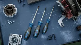 Tre unbrakoskruetrækkere på en metalarbejdsbænk ved siden af ​​bolte og maskindele.
