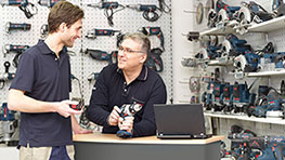 To personer står ved et bord med Bosch værktøj og en bærbar computer i baggrunden.