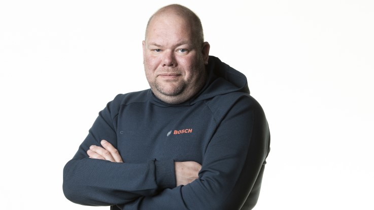 En mand står med armene kors og bærer en blå Bosch hættetrøje.