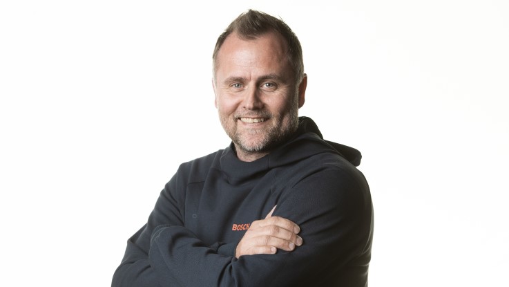 En smilende mand i en sort trøje med Bosch-logo står med armene over kors.