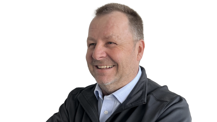 En mand smiler, iført en sort jakke og en lys skjorte.