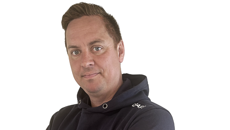 En mand med kort hår bærer en mørk trøje og kigger direkte ind i kameraet.