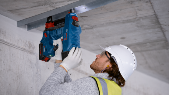 En mand bruger en blå Bosch Professional akku-nailer under en betonloft.