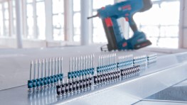 En blå Bosch Professional hæftepistol står bag en række hæfteklammer på en metaloverflade.