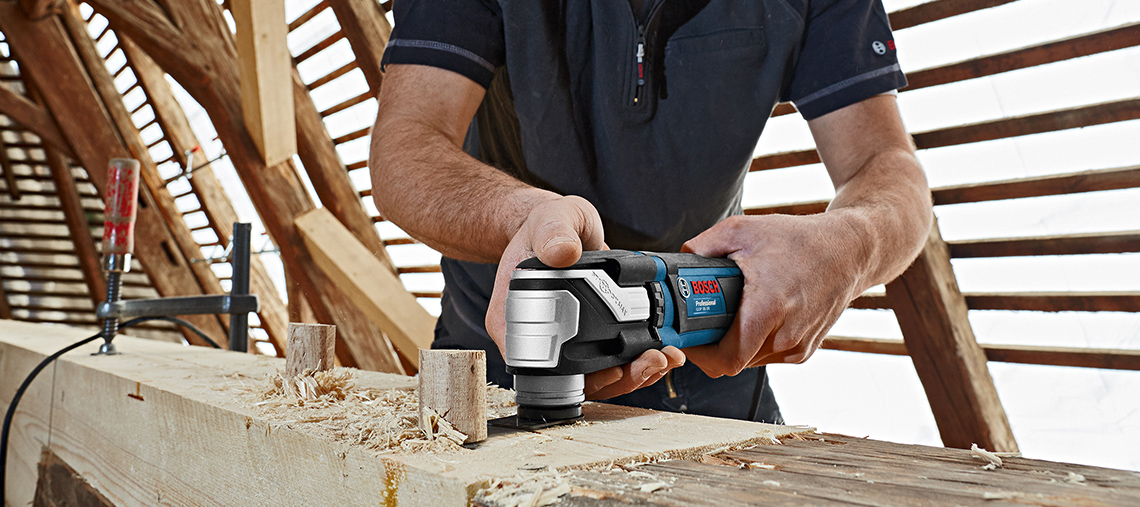 En mand arbejder med en Bosch Professional værktøj på en træoverflade.