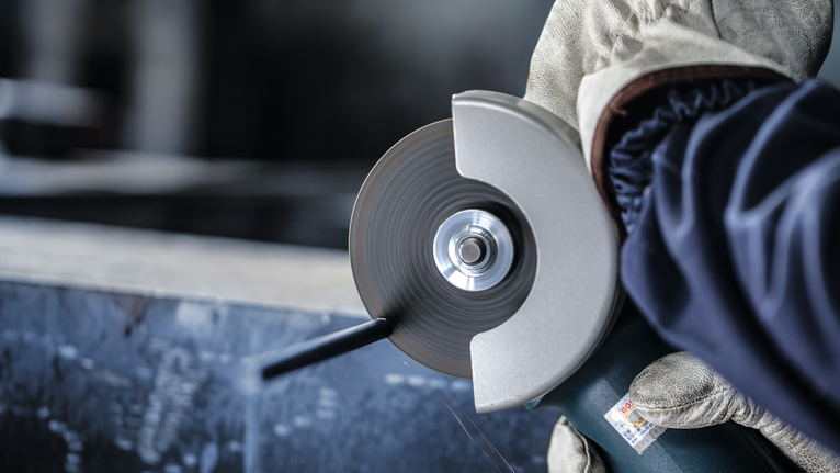 الشخص الذي يرتدي معدات السلامة يستخدم آلة الطحن الزاوية لقطع المعدن.