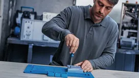 يقوم شخص بتجميع قطعة معدنية باستخدام مفك براغي على طاولة عمل.