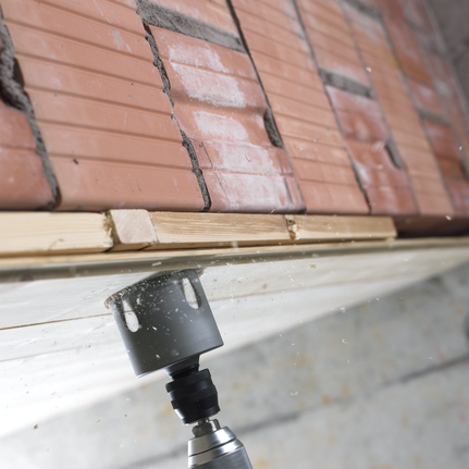 Hole saw drilling through wood beneath a row of stacked bricks.