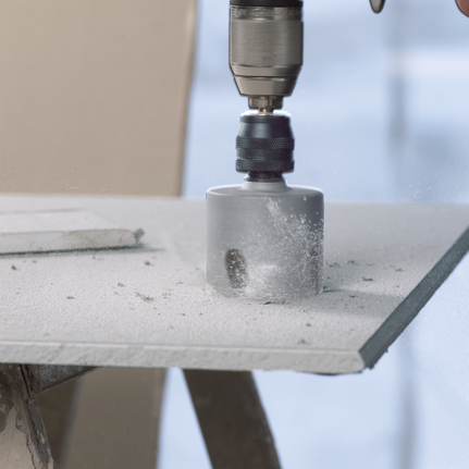 A hole saw drills through a cement board with dust scattering.
