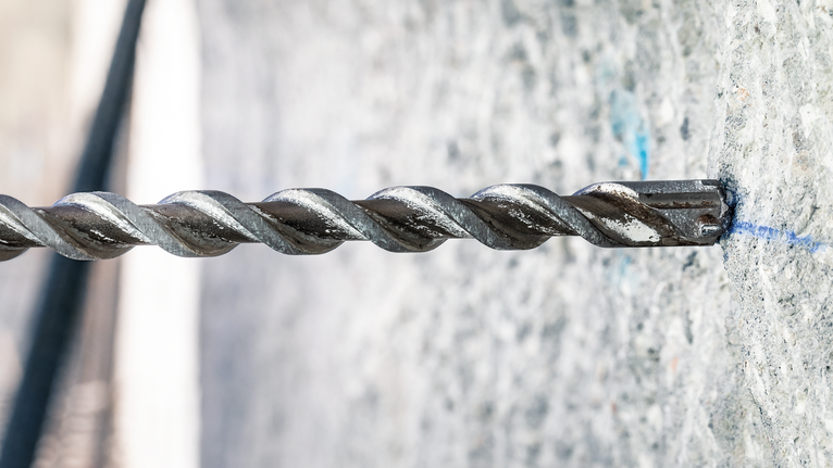 Rotary hammer drill bit making a hole in a concrete wall.