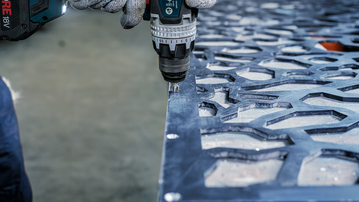 Person wearing safety equipment drills into a patterned metal sheet.