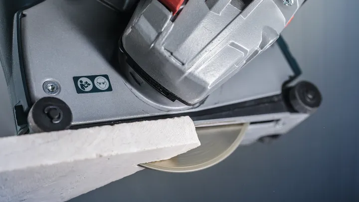 Tile saw cutting a white tile, safety symbols visible on the tool.