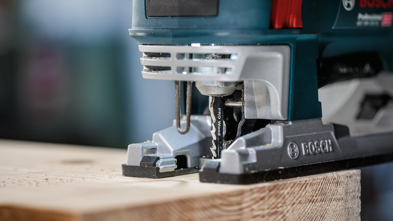 Jigsaw cutting through a wooden plank in a workshop setting.