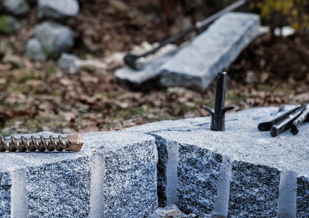 Masonry drill bit and stone splitting tools placed on cut granite blocks.