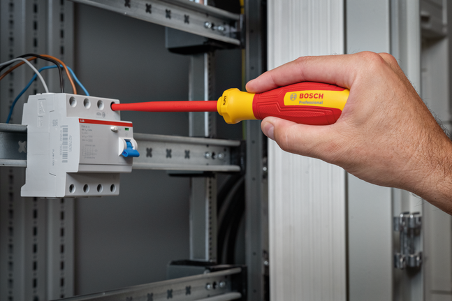 Person using an insulated screwdriver to adjust wiring in an electrical panel.