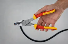 Person cutting a black cable with insulated side cutters.