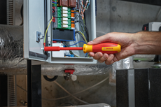 Person uses an insulated screwdriver to adjust wiring inside an electrical control panel.