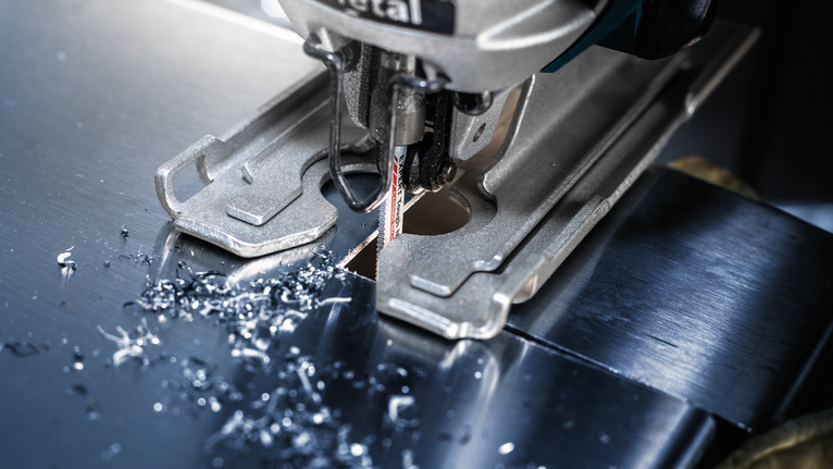 Jigsaw cutting a sheet of metal, small metal shavings scattered around the blade.