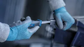 Person wearing safety equipment tightens a metal part with a screwdriver.