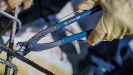 Person wearing safety equipment cuts wire on a metal frame with pliers.