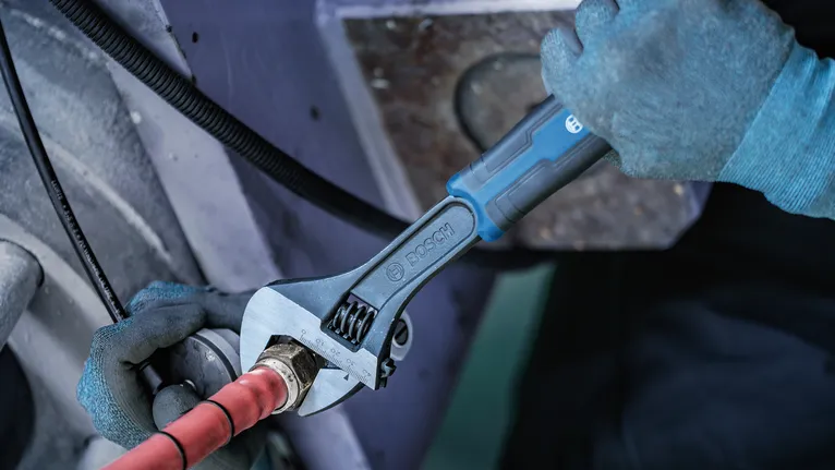 Person wearing safety equipment tightens a pipe fitting with an adjustable wrench.