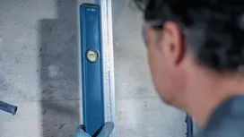 Person wearing safety equipment checks alignment with a spirit level against a wall.