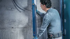Person wearing safety equipment checks wall alignment with a spirit level.