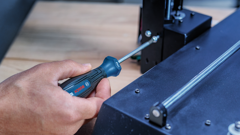 Person tightens a screw on a machine using a screwdriver.
