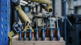 A row of screwdrivers is arranged on a wooden surface in front of industrial machinery.