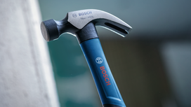 A steel claw hammer with a blue handle held upright against a blurred background.