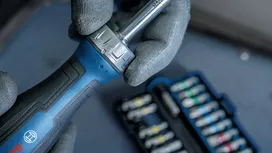 Person wearing safety equipment holds a ratchet handle near a socket set.