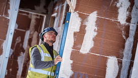 Person wearing safety equipment checks wall alignment with a spirit level.