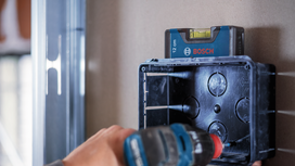 Person uses a drill to install an electrical box, small level placed on top.