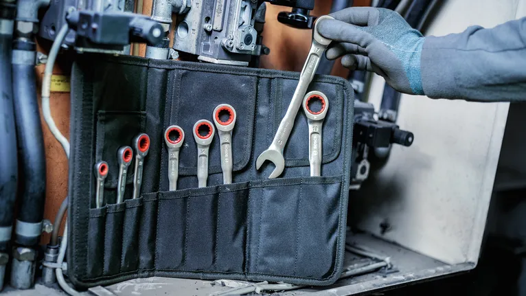Person wearing safety equipment selecting a ratcheting wrench from a tool pouch.