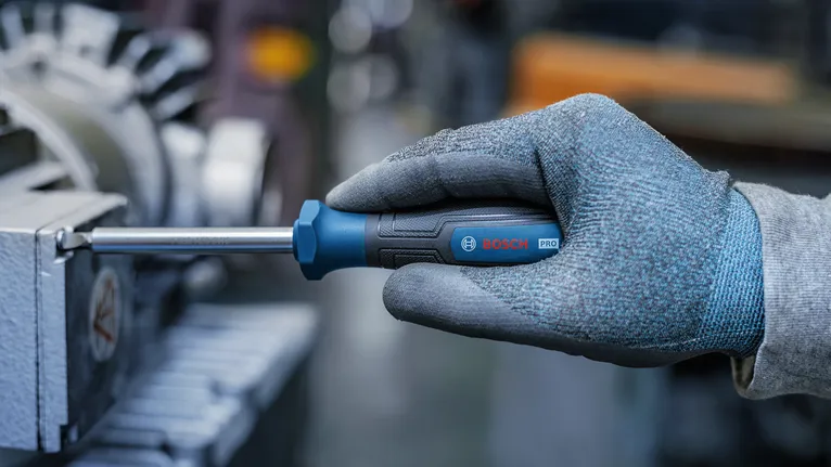 Person wearing safety equipment tightens a machine part using a screwdriver.