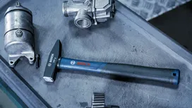 Metal hammer on a workbench beside engine parts.