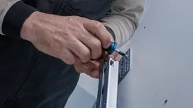 Person uses a screwdriver to secure a metal bracket to a wall.